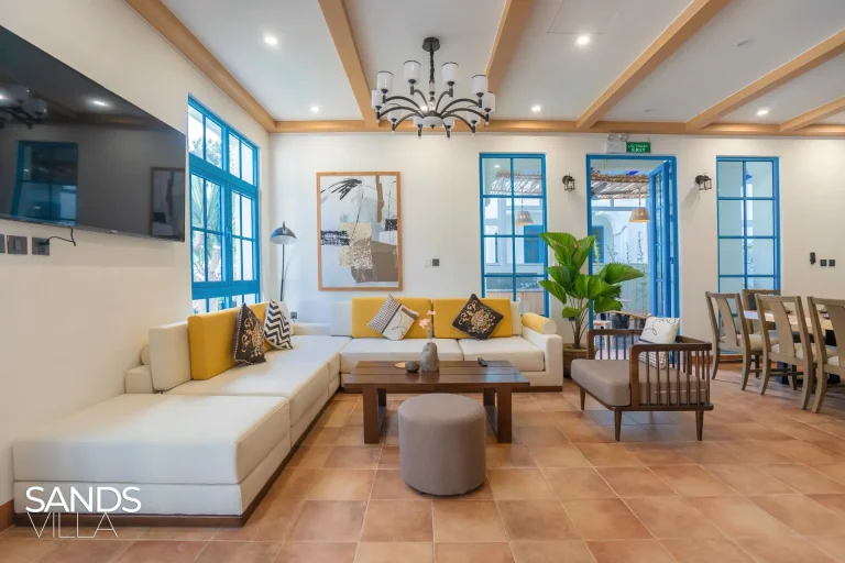 Phòng khách Sands Villa C6-16 với sofa chữ L nệm vàng, tivi treo tường và đèn chùm