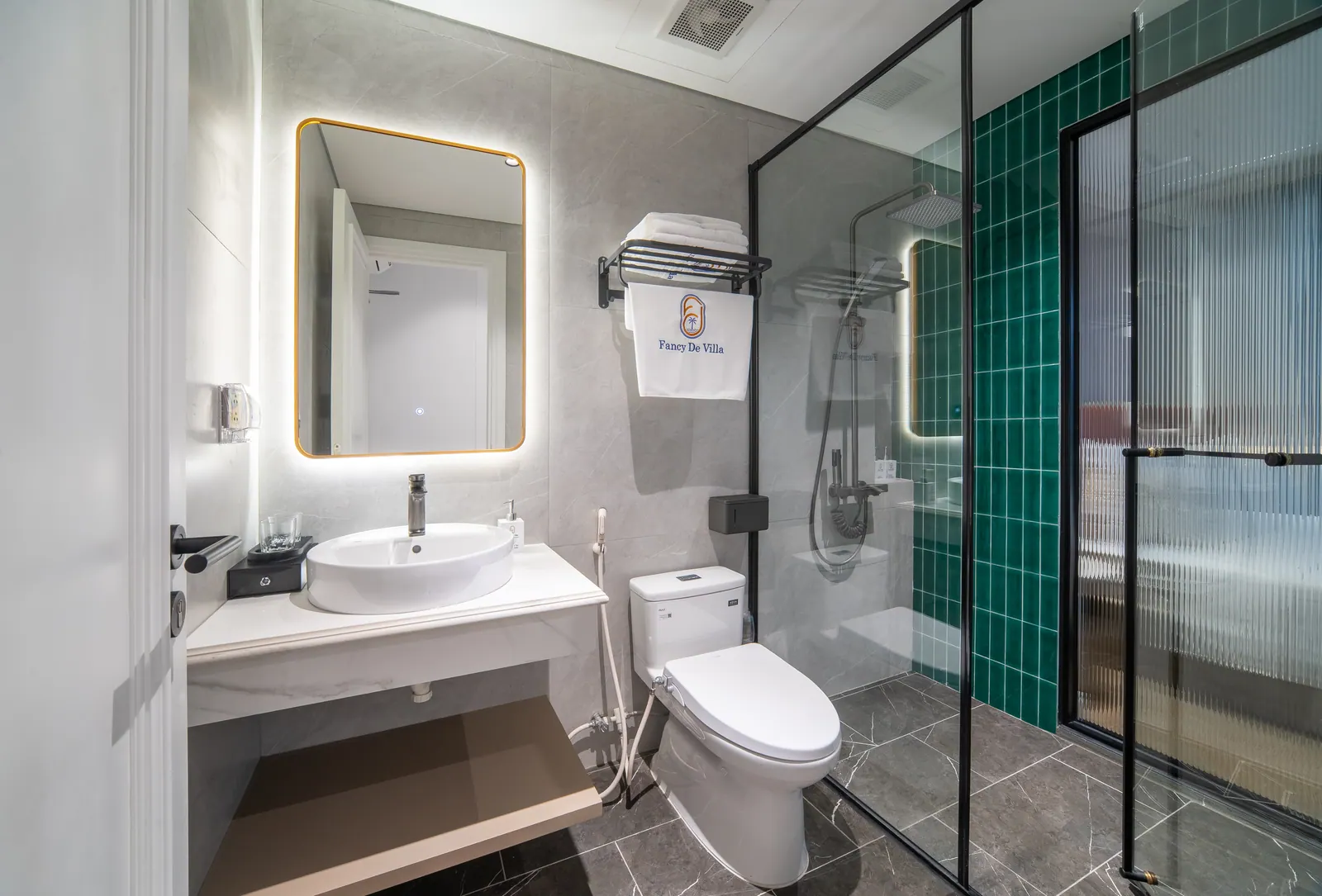 Phòng tắm có lavabo trắng, gạch ốp xanh và vách kính